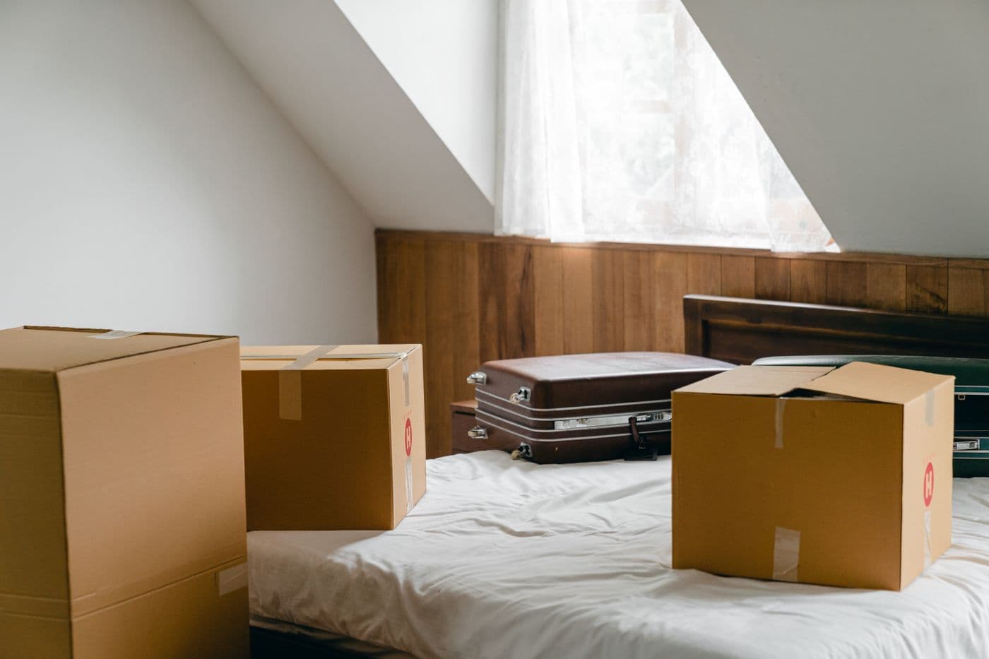 Umzugskartons und alte Koffer auf einem Bett unter einer Dachschräge